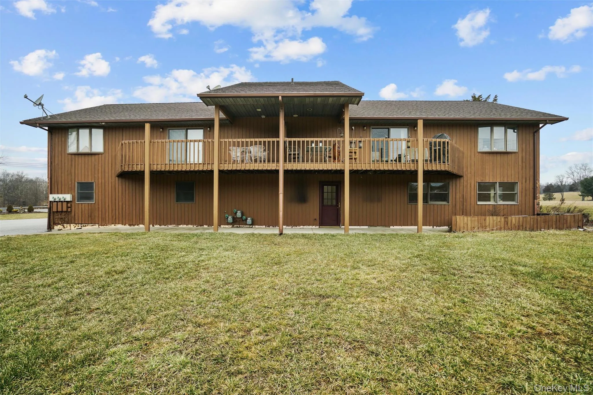 Back of property with a wooden deck, roof with shingles, and a lawn Back of property with a wooden deck, roof with shingles, and a lawn