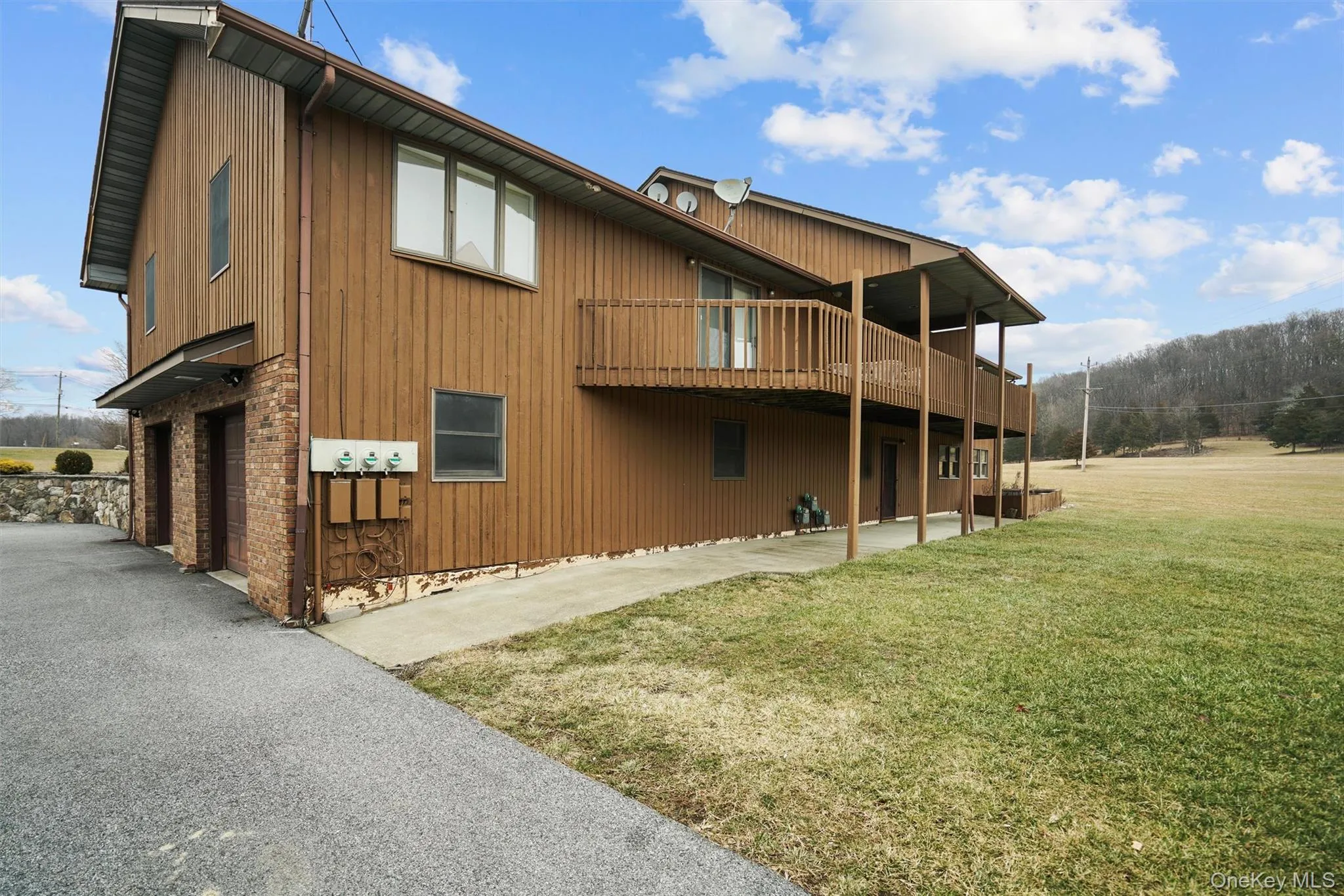 View of side of property featuring a garage, a deck, a lawn, a wooded view, and driveway View of side of property featuring a garage, a deck, a lawn, a wooded view, and driveway