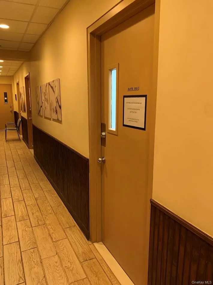 Office entrance, view from Hallway-Hall with a wainscoted wall, wood walls, a drop ceiling, and light wood finished floors Office entrance, view from Hallway-Hall with a wainscoted wall, wood walls, a drop ceiling, and light wood finished floors