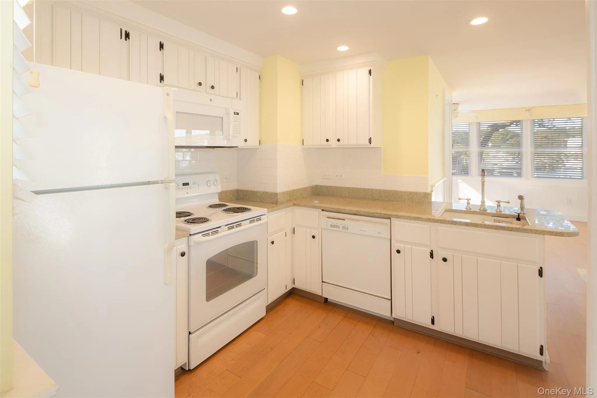 Kitchen featuring white appliances, a peninsula, light wood-style flooring, recessed lighting, and decorative backsplash Kitchen featuring white appliances, a peninsula, light wood-style flooring, recessed lighting, and decorative backsplash