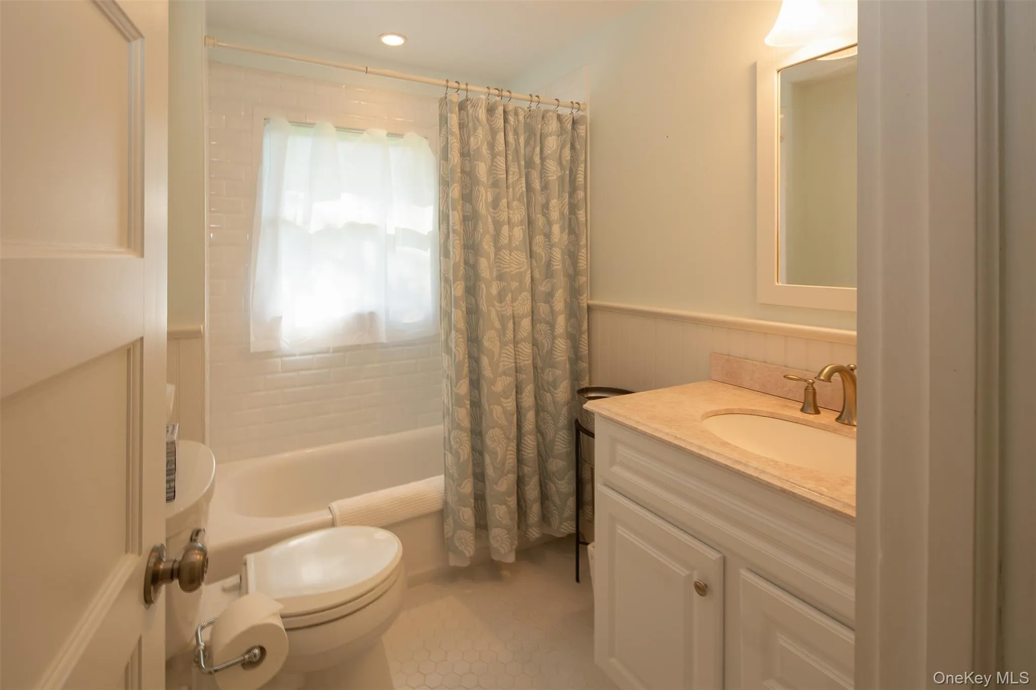 Bathroom featuring shower / bathtub combination with curtain, vanity, a wainscoted wall, and light tile patterned floors Bathroom featuring shower / bathtub combination with curtain, vanity, a wainscoted wall, and light tile patterned floors