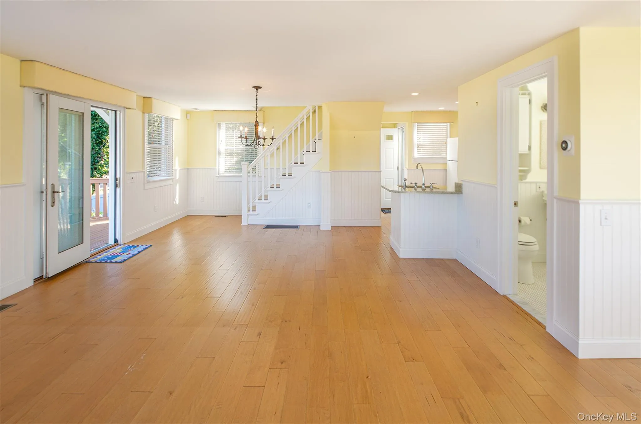 Unfurnished dining area featuring a wainscoted wall, light wood-style flooring, a chandelier, and stairway Unfurnished dining area featuring a wainscoted wall, light wood-style flooring, a chandelier, and stairway