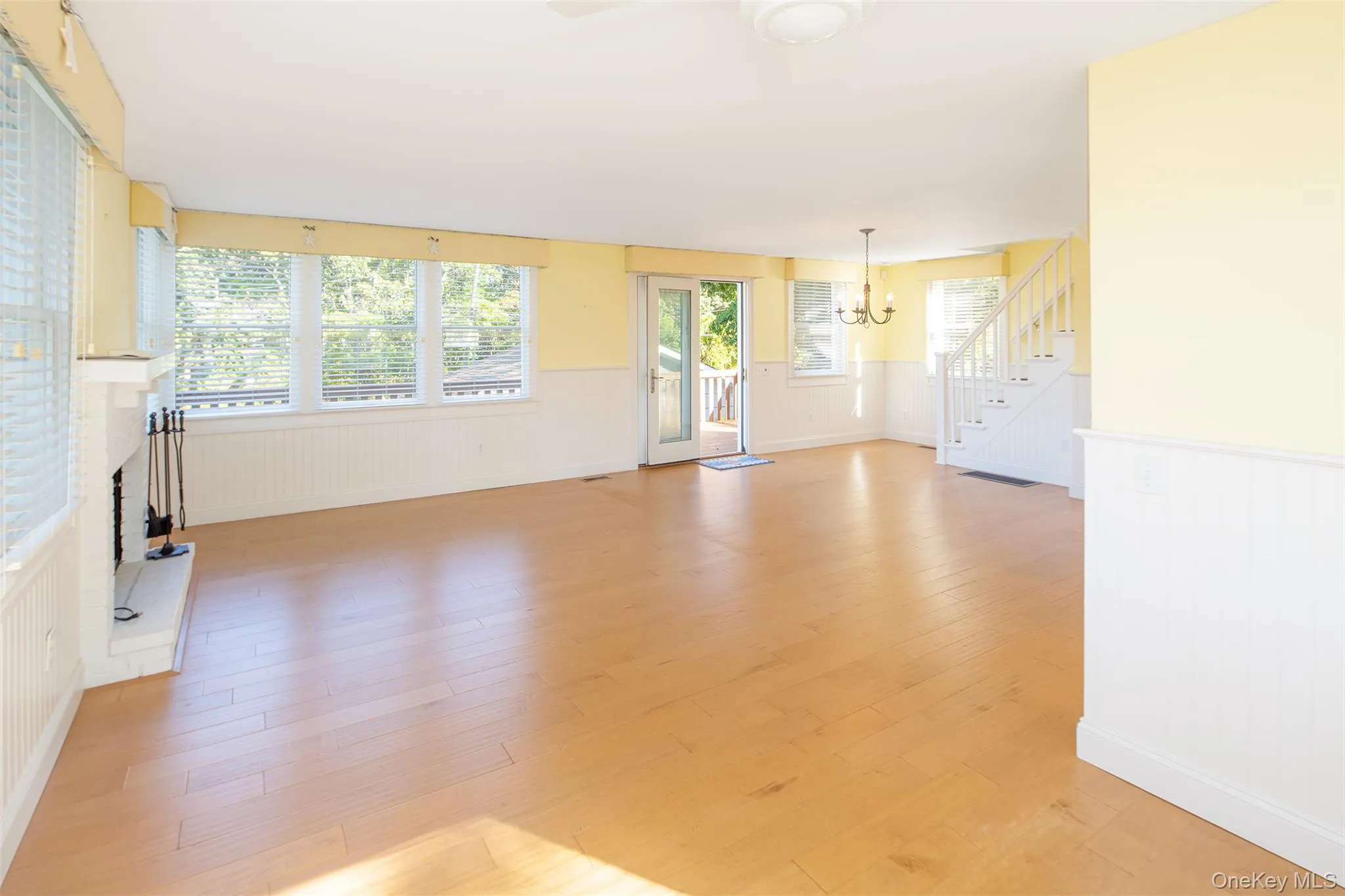 Unfurnished living room with a wainscoted wall, stairway, a brick fireplace, light wood-type flooring, and a chandelier Unfurnished living room with a wainscoted wall, stairway, a brick fireplace, light wood-type flooring, and a chandelier