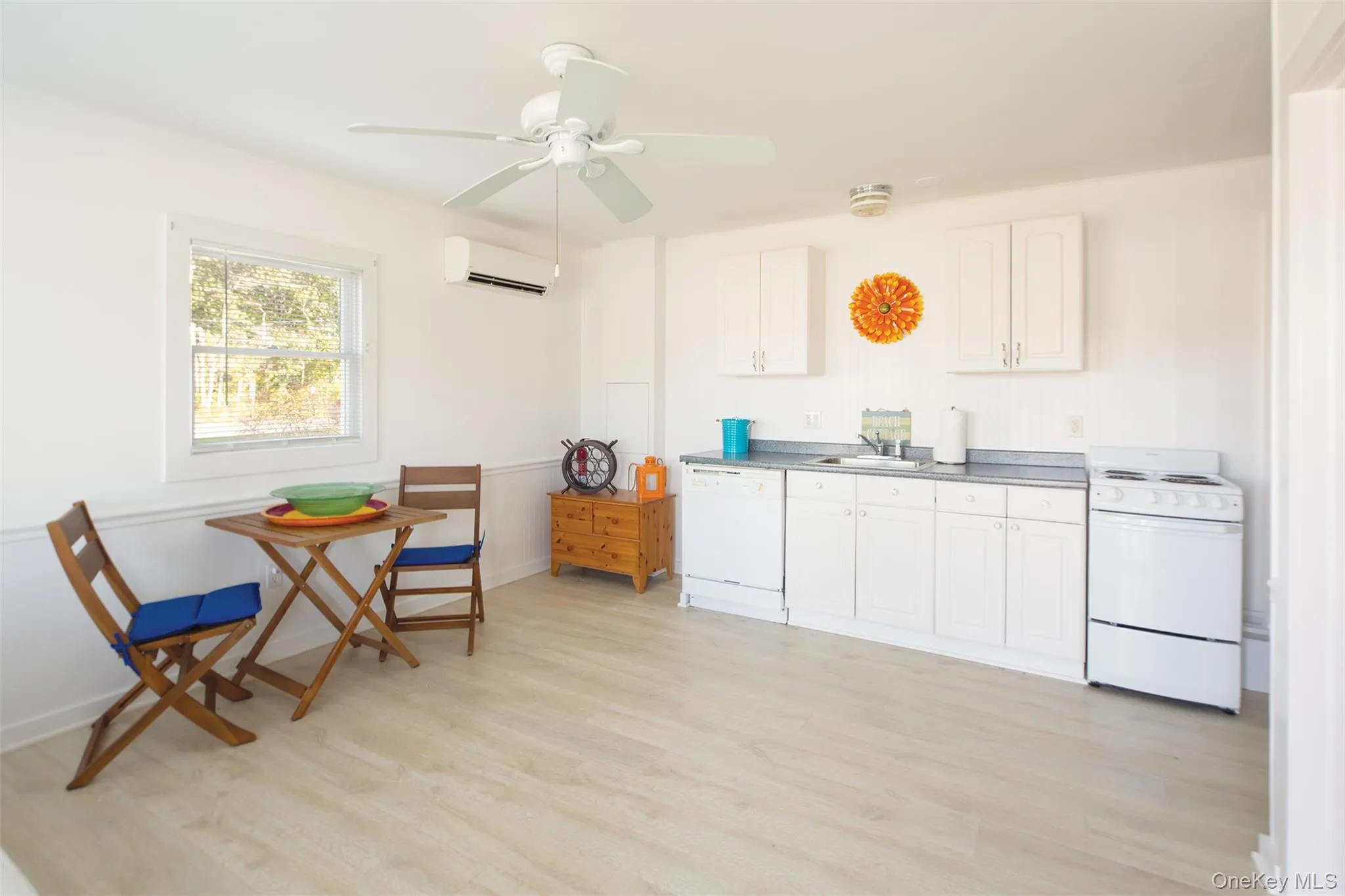 Kitchen with white appliances, light wood finished floors, white cabinetry, ceiling fan, and a wall mounted air conditioner Kitchen with white appliances, light wood finished floors, white cabinetry, ceiling fan, and a wall mounted air conditioner