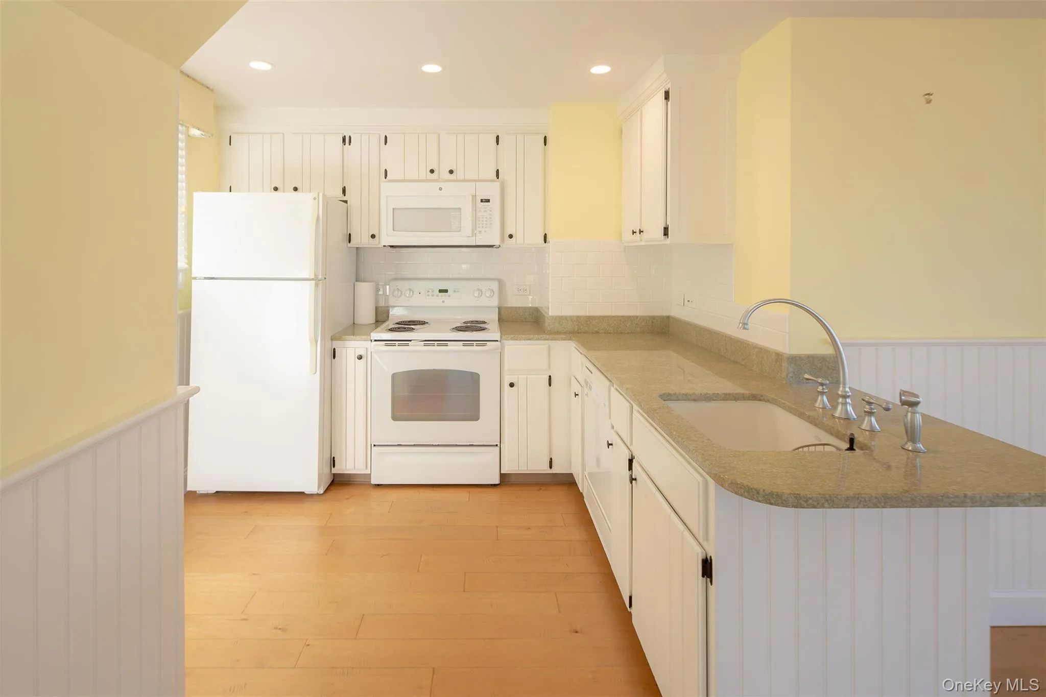 Kitchen with a wainscoted wall, white appliances, light stone countertops, decorative backsplash, and light wood-style floors Kitchen with a wainscoted wall, white appliances, light stone countertops, decorative backsplash, and light wood-style floors