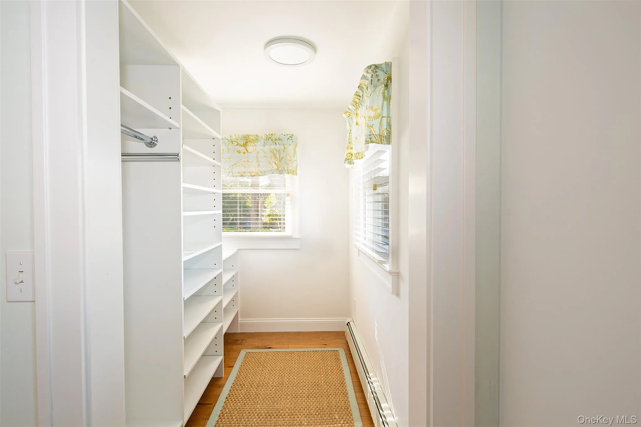 Walk in closet featuring light wood finished floors and baseboard heating Walk in closet featuring light wood finished floors and baseboard heating