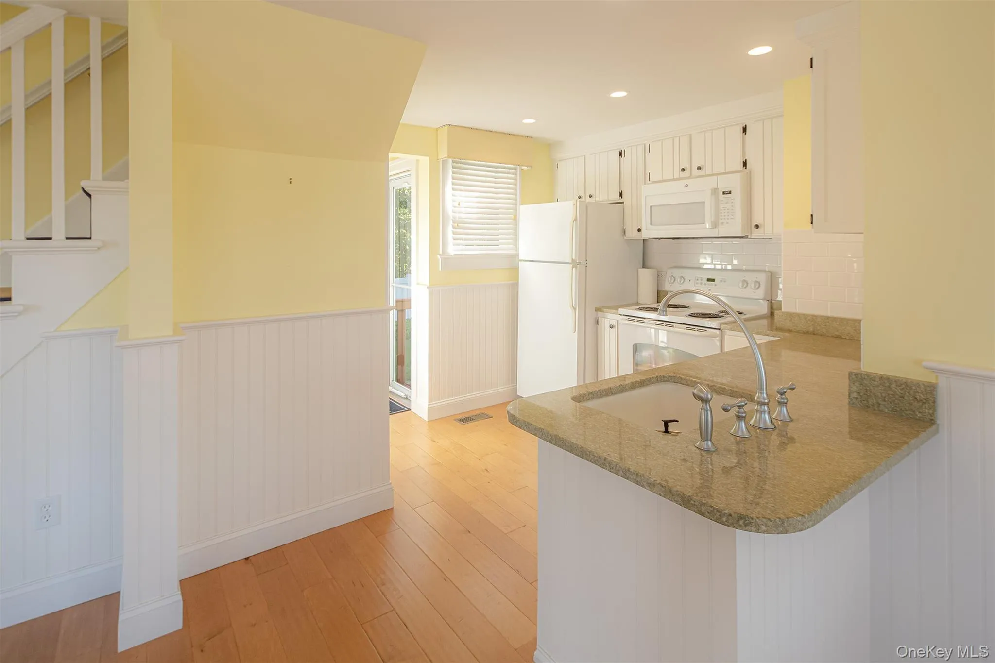Kitchen with wainscoting, white appliances, light wood-style flooring, light stone counters, and tasteful backsplash Kitchen with wainscoting, white appliances, light wood-style flooring, light stone counters, and tasteful backsplash