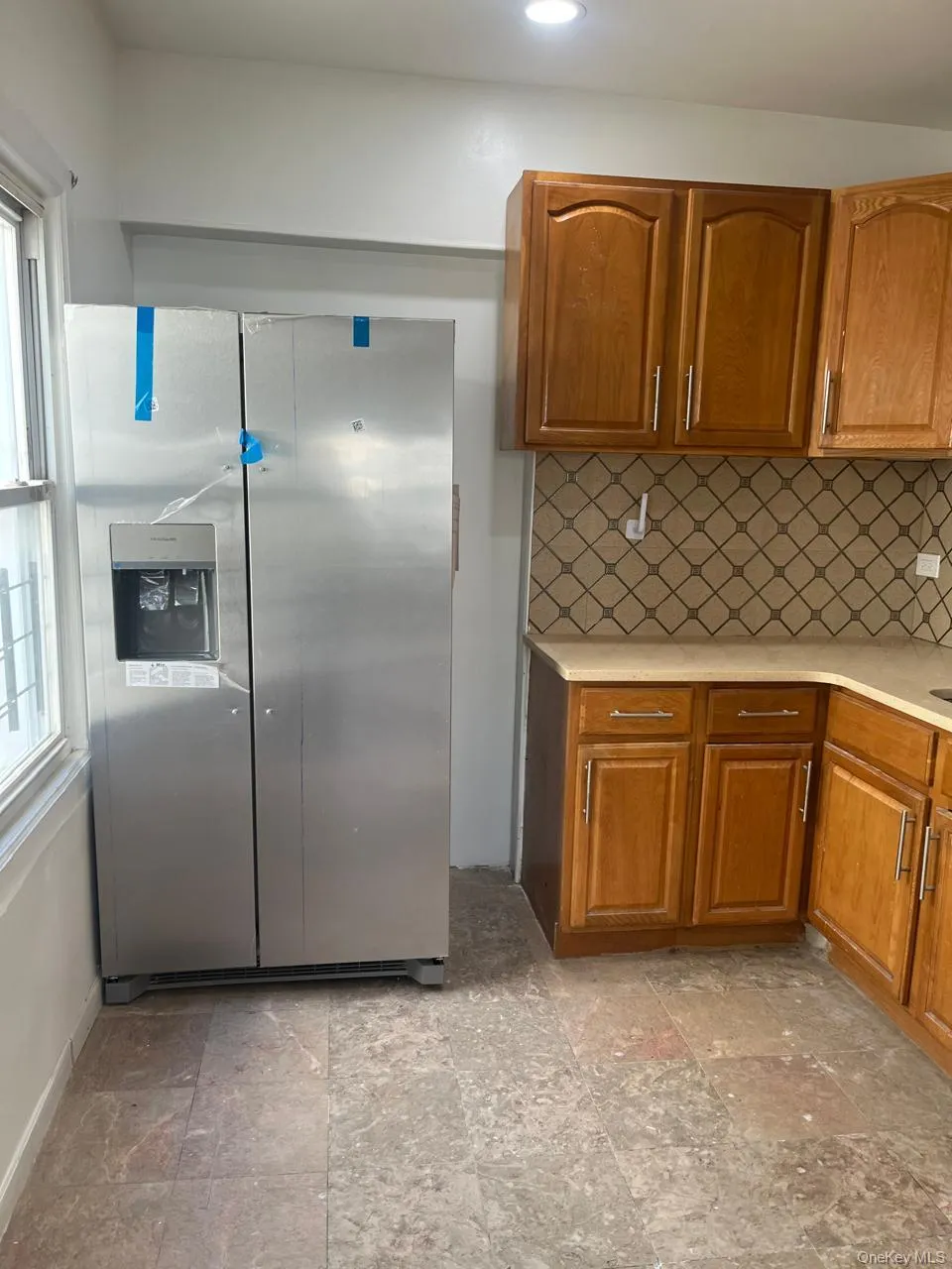 Kitchen with brown cabinetry, stainless steel fridge with ice dispenser, tasteful backsplash, light stone finish floors, and recessed lighting Kitchen with brown cabinetry, stainless steel fridge with ice dispenser, tasteful backsplash, light stone finish floors, and recessed lighting