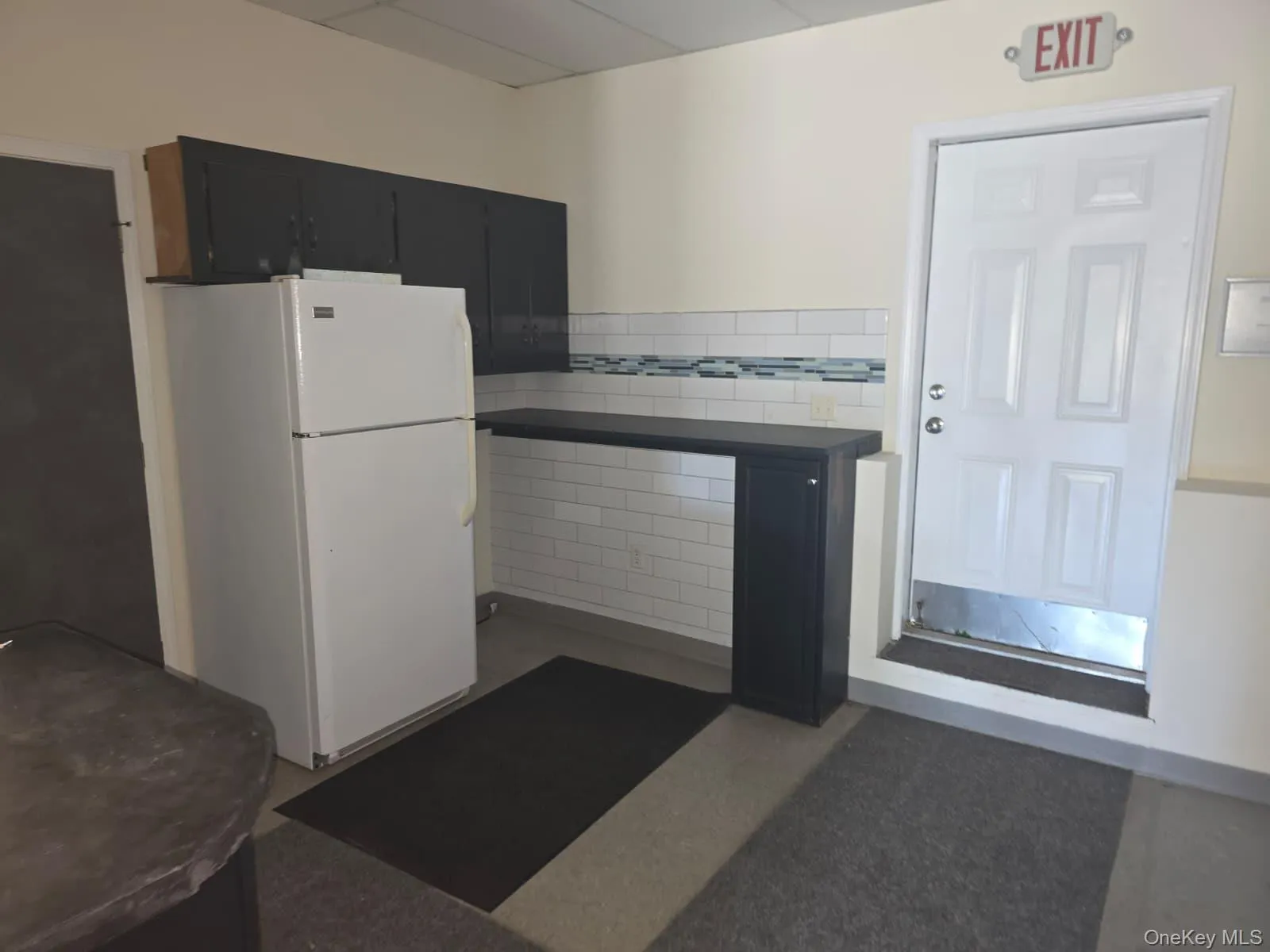 Kitchen featuring dark cabinets, tile walls, freestanding refrigerator, a drop ceiling, and a wainscoted wall Kitchen featuring dark cabinets, tile walls, freestanding refrigerator, a drop ceiling, and a wainscoted wall
