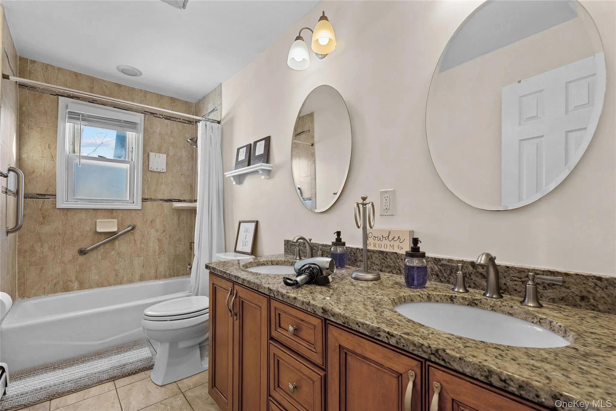 Full bathroom featuring shower / bath combo with shower curtain, double vanity, and light tile patterned flooring Full bathroom featuring shower / bath combo with shower curtain, double vanity, and light tile patterned flooring