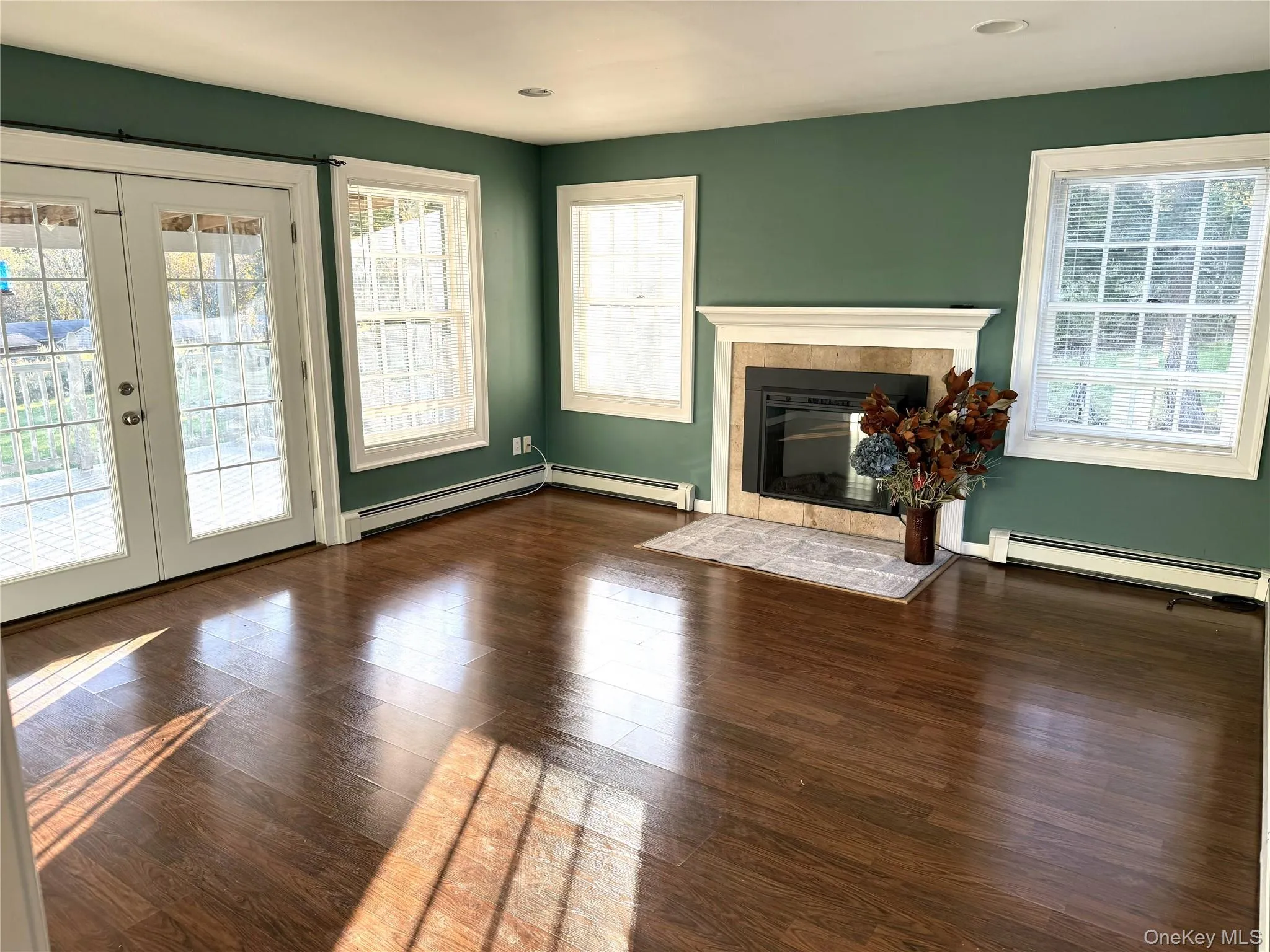 Unfurnished living room featuring a fireplace, dark wood-style floors, a baseboard heating unit, and french doors Unfurnished living room featuring a fireplace, dark wood-style floors, a baseboard heating unit, and french doors