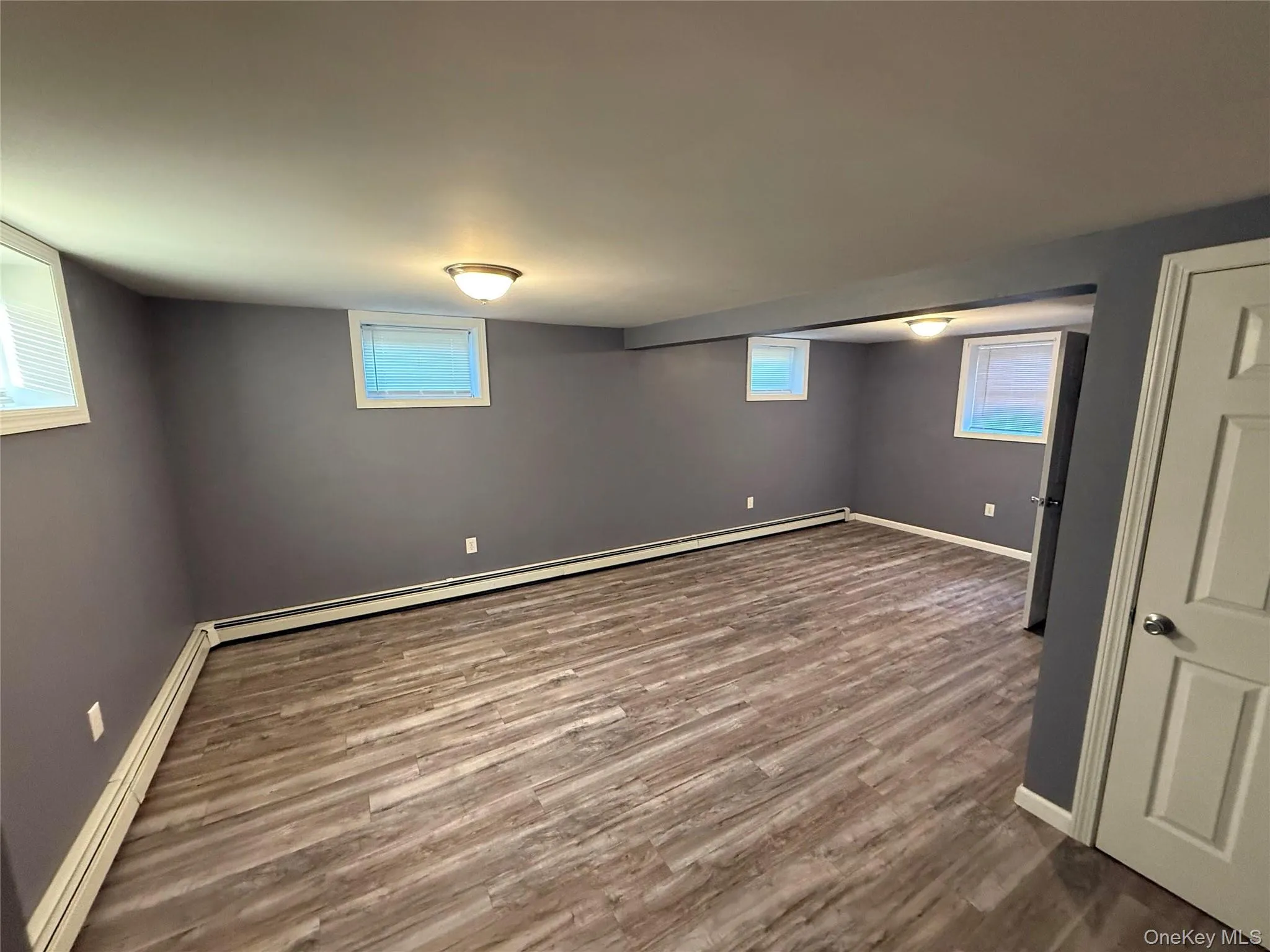 Below grade area with a baseboard heating unit, dark wood finished floors, and plenty of natural light Below grade area with a baseboard heating unit, dark wood finished floors, and plenty of natural light