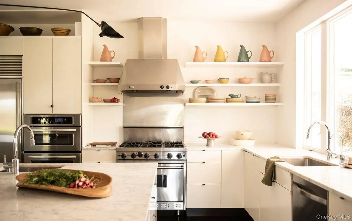 Kitchen with open shelves, wall chimney range hood, high end appliances, light stone counters, and modern cabinets Kitchen with open shelves, wall chimney range hood, high end appliances, light stone counters, and modern cabinets