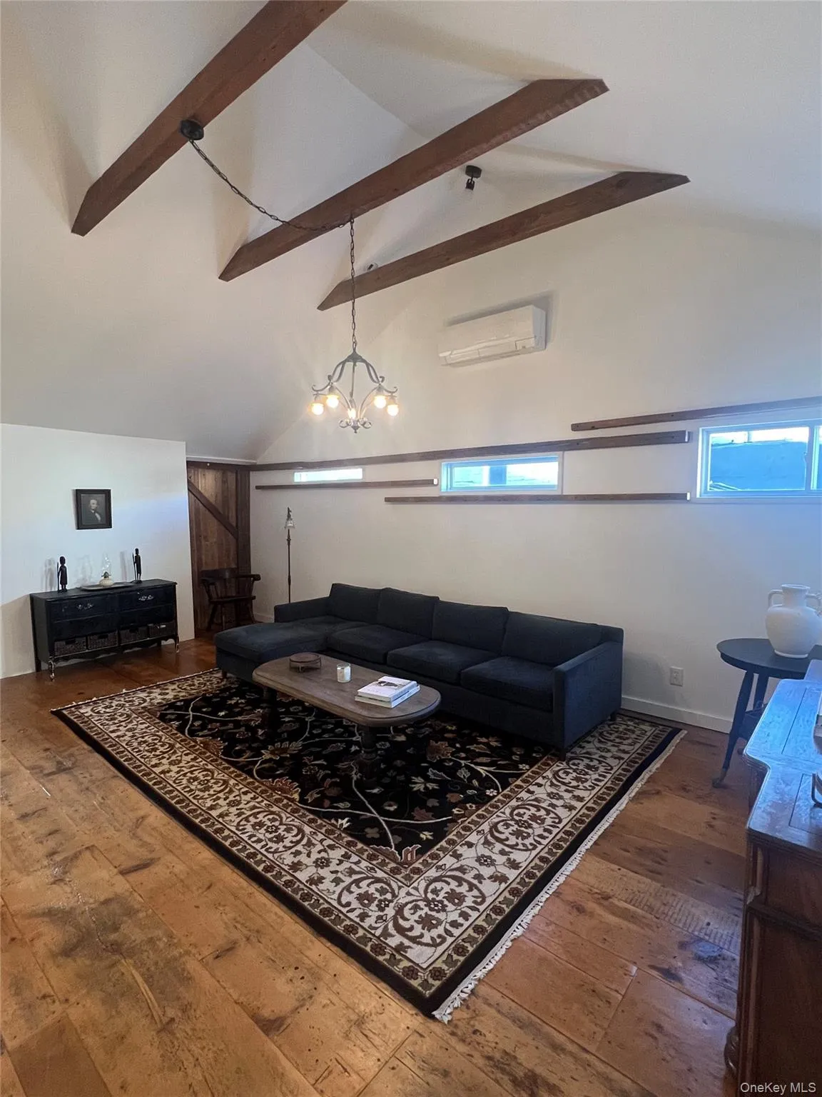 Living area with wood flooring, beamed ceiling, a wall unit AC, high vaulted ceiling, and a chandelier Living area with wood flooring, beamed ceiling, a wall unit AC, high vaulted ceiling, and a chandelier