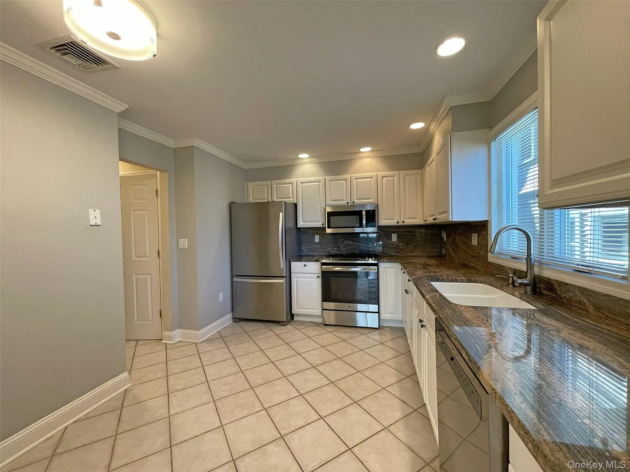Kitchen with appliances with stainless steel finishes, backsplash, light tile patterned floors, dark stone countertops, and ornamental molding Kitchen with appliances with stainless steel finishes, backsplash, light tile patterned floors, dark stone countertops, and ornamental molding