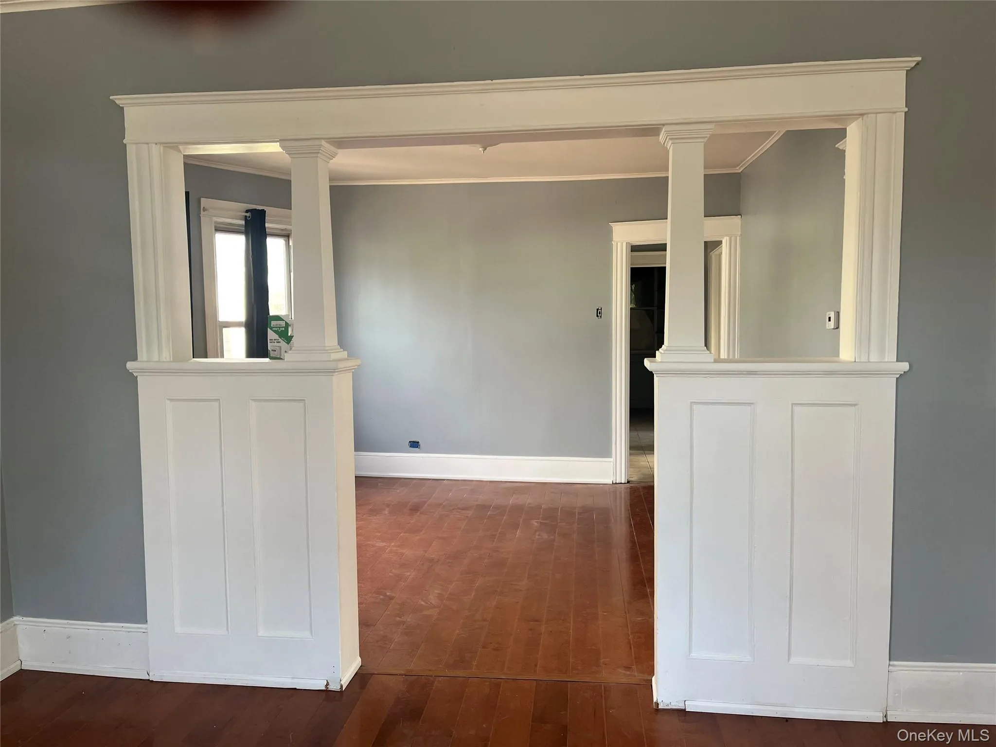 Spare room with dark wood-style flooring, ornate columns, and ornamental molding Spare room with dark wood-style flooring, ornate columns, and ornamental molding