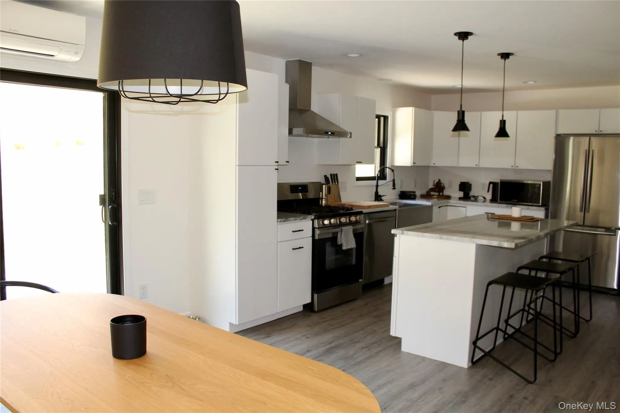 Kitchen with wall chimney range hood, appliances with stainless steel finishes, white cabinets, a kitchen bar, and a wall mounted AC Kitchen with wall chimney range hood, appliances with stainless steel finishes, white cabinets, a kitchen bar, and a wall mounted AC