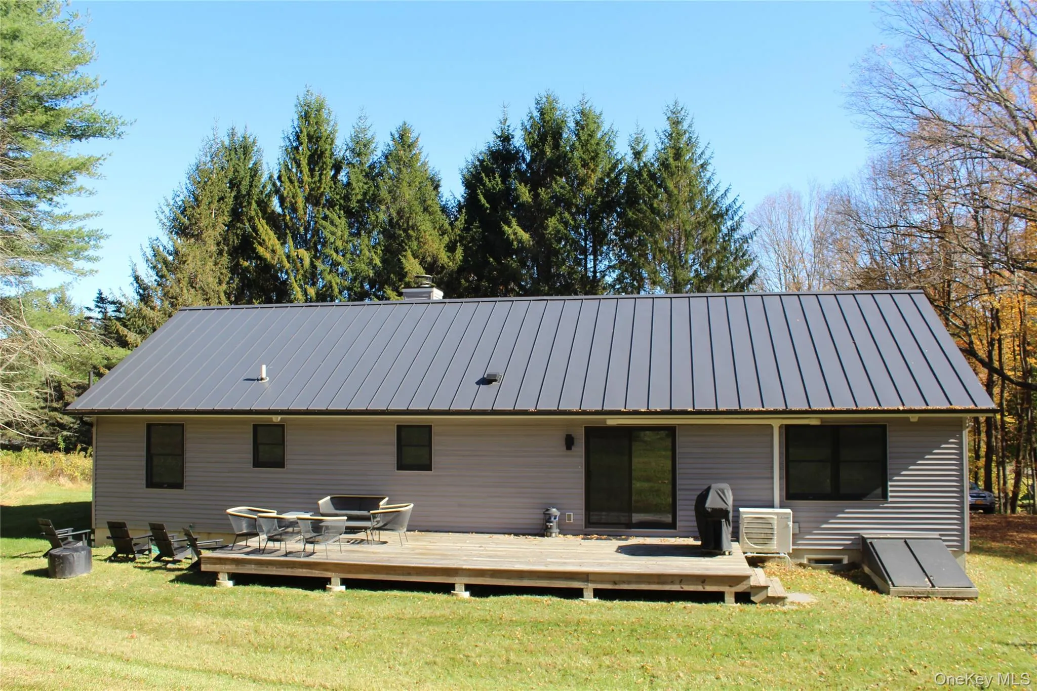 Back of property featuring a yard, a deck, and a metal roof Back of property featuring a yard, a deck, and a metal roof
