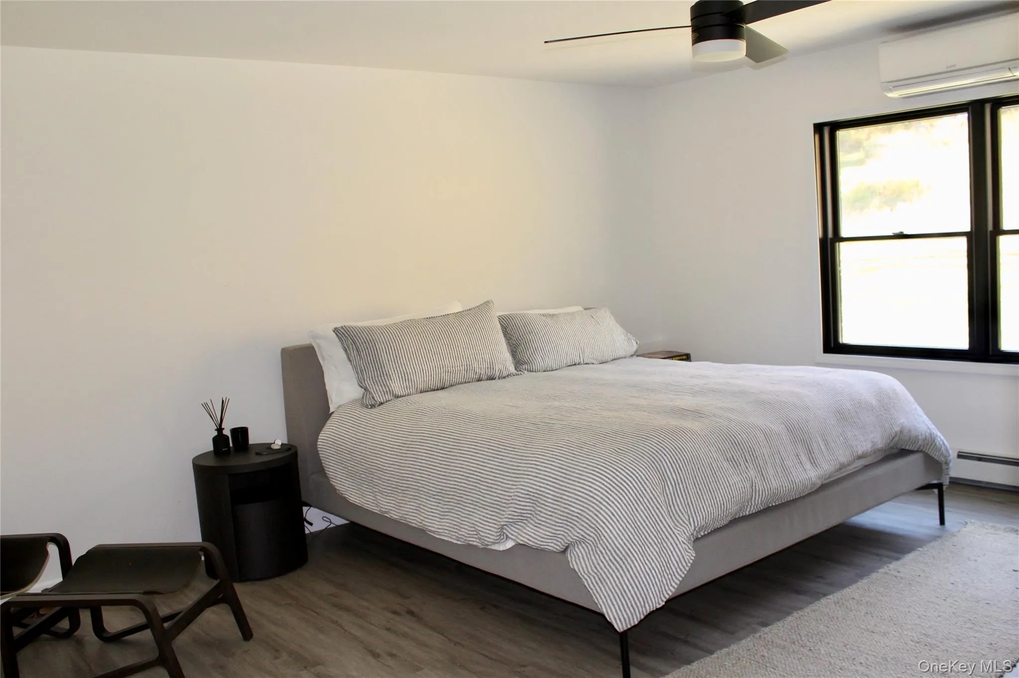 Bedroom with wood finished floors, an AC wall unit, a ceiling fan, and baseboard heating Bedroom with wood finished floors, an AC wall unit, a ceiling fan, and baseboard heating