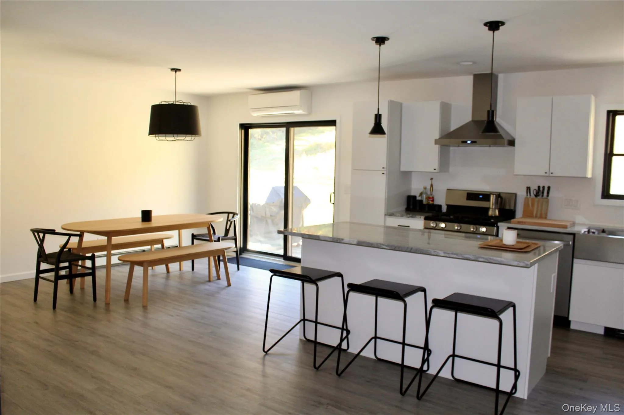 Kitchen with wall chimney exhaust hood, a breakfast bar, stainless steel appliances, decorative light fixtures, and white cabinets Kitchen with wall chimney exhaust hood, a breakfast bar, stainless steel appliances, decorative light fixtures, and white cabinets
