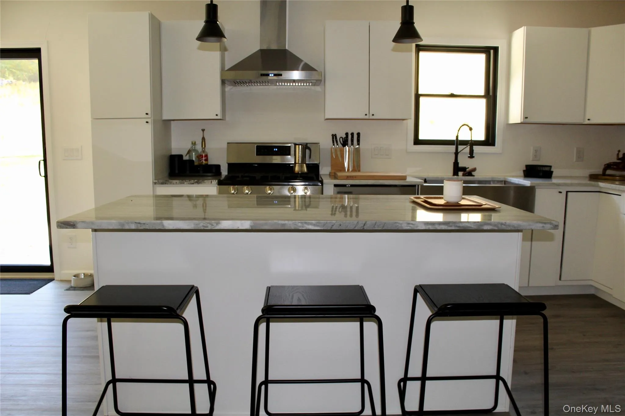 Kitchen featuring a kitchen bar, wall chimney exhaust hood, a center island, stainless steel gas stove, and white cabinetry Kitchen featuring a kitchen bar, wall chimney exhaust hood, a center island, stainless steel gas stove, and white cabinetry