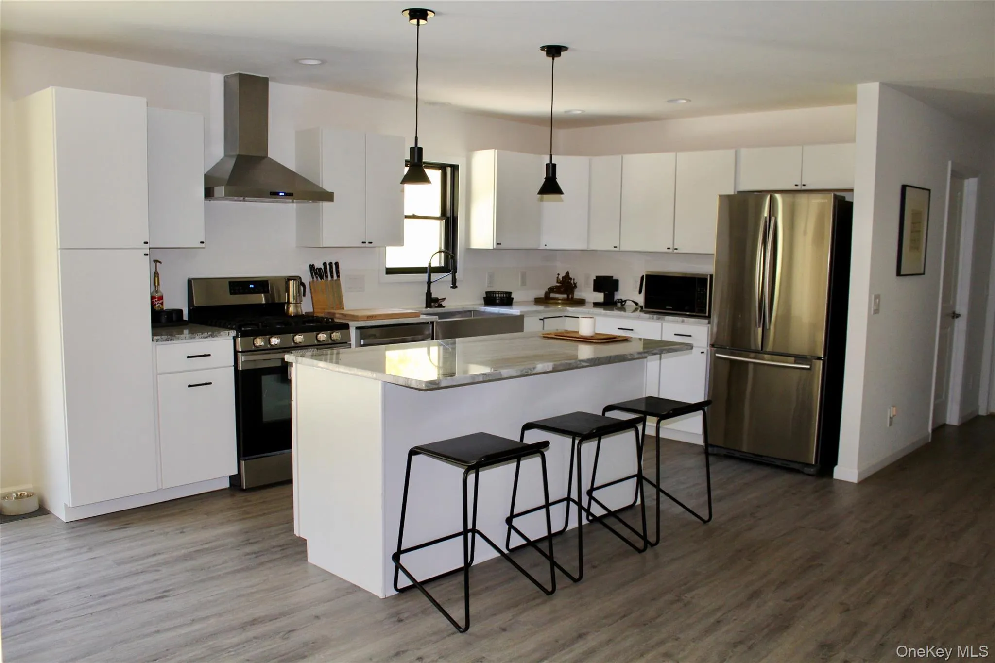 Kitchen featuring appliances with stainless steel finishes, wall chimney range hood, decorative light fixtures, white cabinetry, and light stone countertops Kitchen featuring appliances with stainless steel finishes, wall chimney range hood, decorative light fixtures, white cabinetry, and light stone countertops