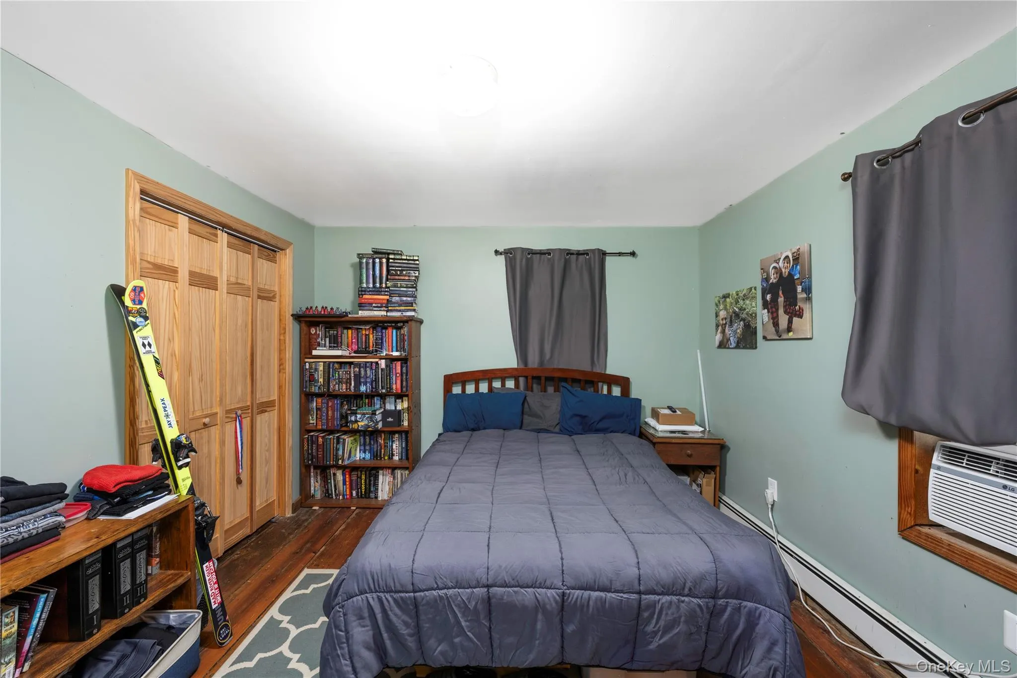 Bedroom with a baseboard heating unit, dark wood-style floors, a closet, and cooling unit Bedroom with a baseboard heating unit, dark wood-style floors, a closet, and cooling unit