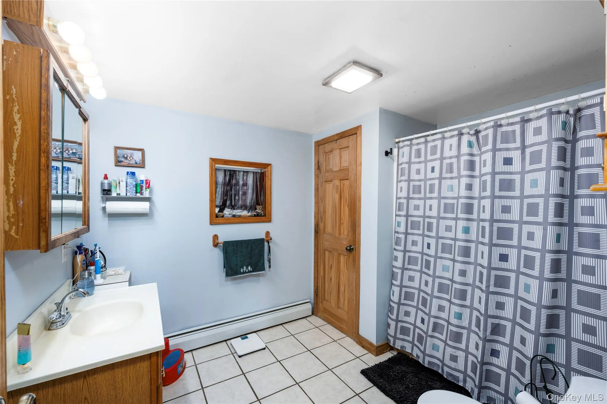 Bathroom featuring baseboard heating, light tile patterned floors, vanity, and a shower with shower curtain Bathroom featuring baseboard heating, light tile patterned floors, vanity, and a shower with shower curtain