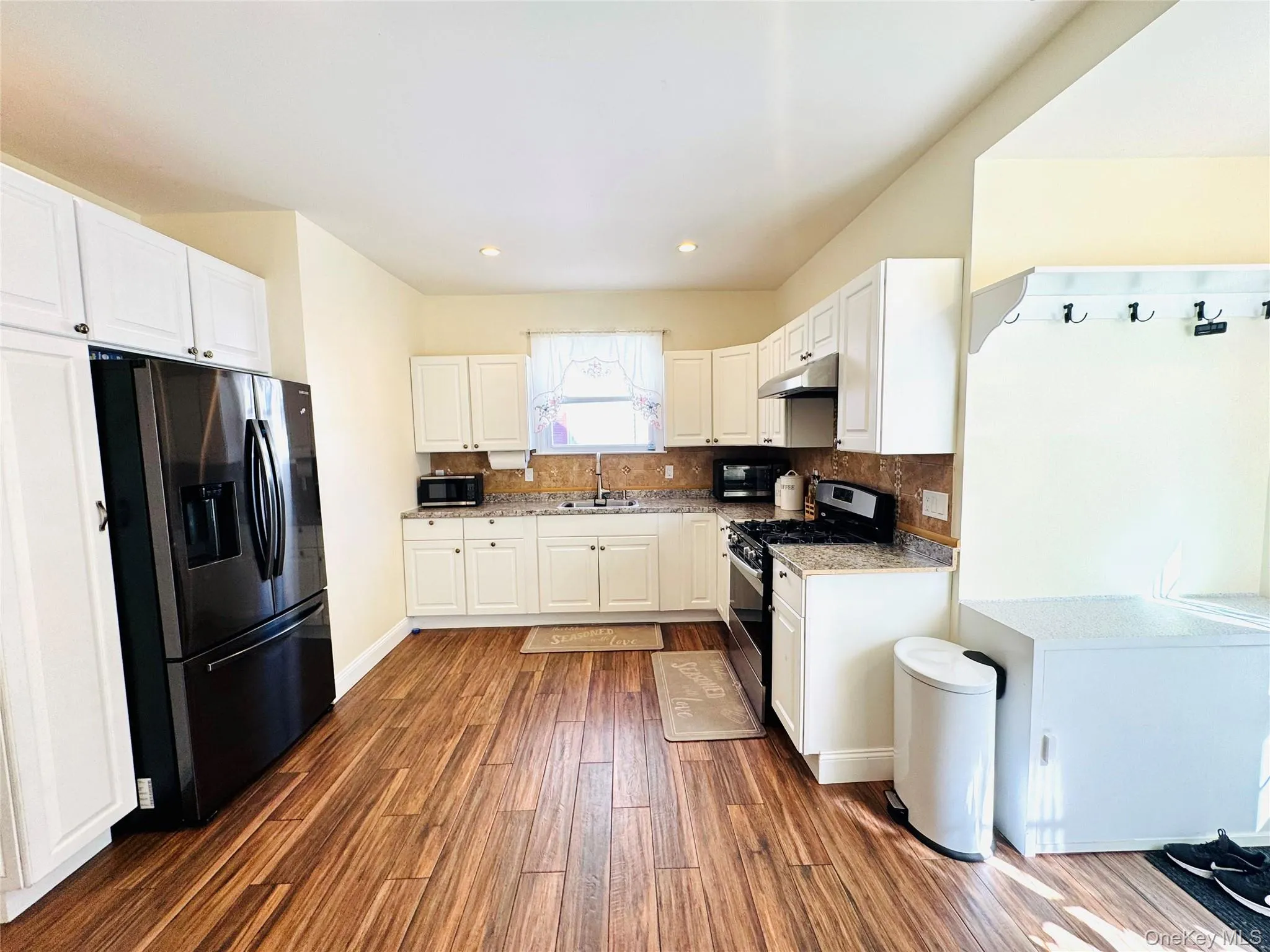 Kitchen with white cabinetry, stainless steel appliances, tasteful backsplash, dark wood finished floors, and light stone countertops Kitchen with white cabinetry, stainless steel appliances, tasteful backsplash, dark wood finished floors, and light stone countertops