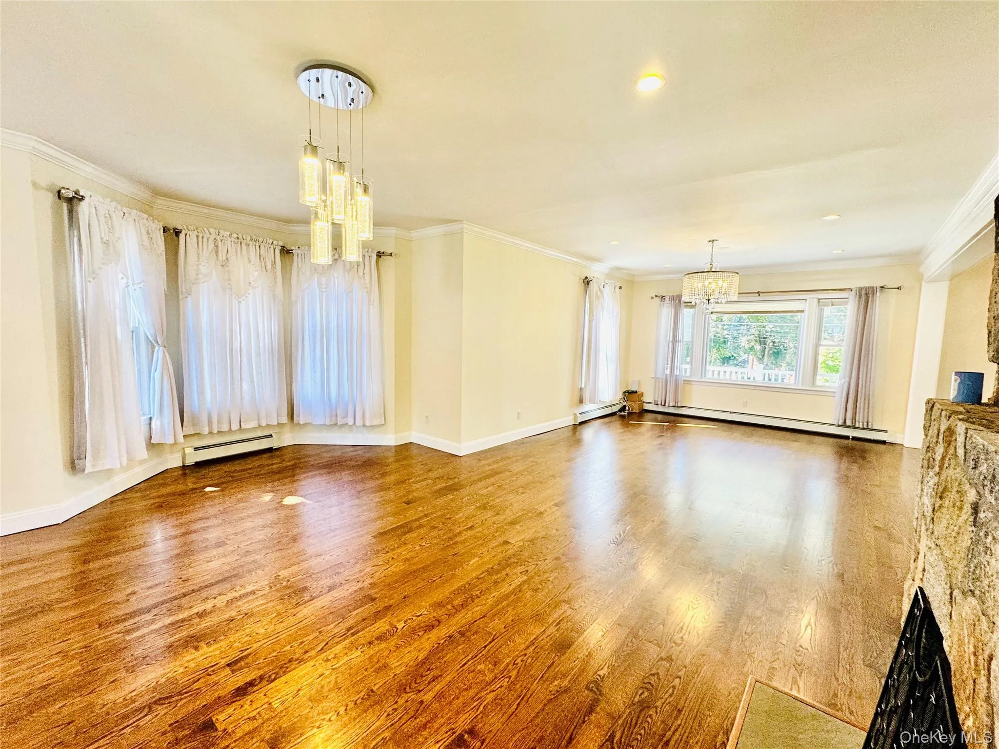 Unfurnished living room featuring a chandelier, ornamental molding, wood finished floors, a baseboard radiator, and recessed lighting Unfurnished living room featuring a chandelier, ornamental molding, wood finished floors, a baseboard radiator, and recessed lighting
