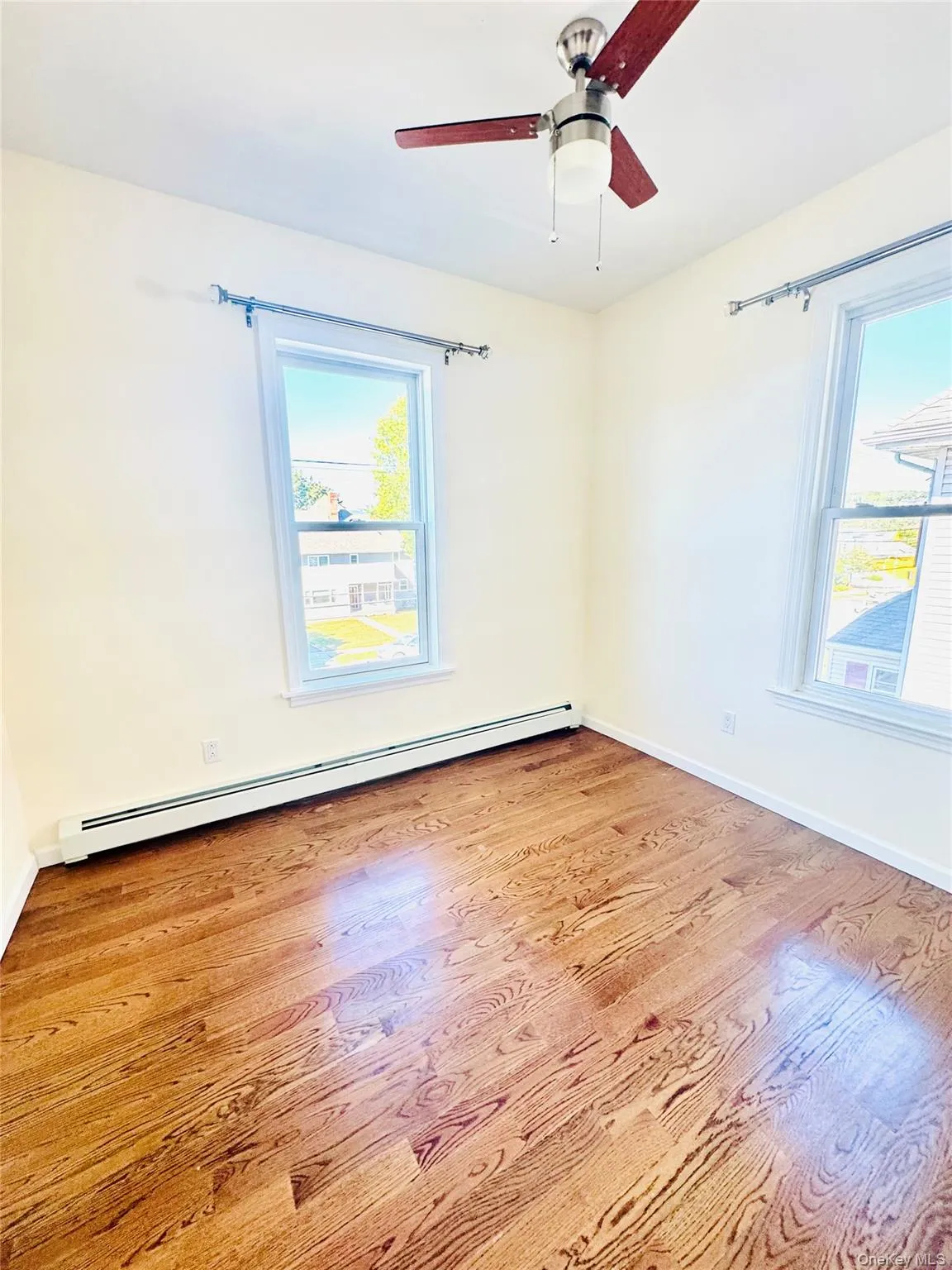 Empty room with a baseboard radiator, light wood-style floors, and a ceiling fan Empty room with a baseboard radiator, light wood-style floors, and a ceiling fan
