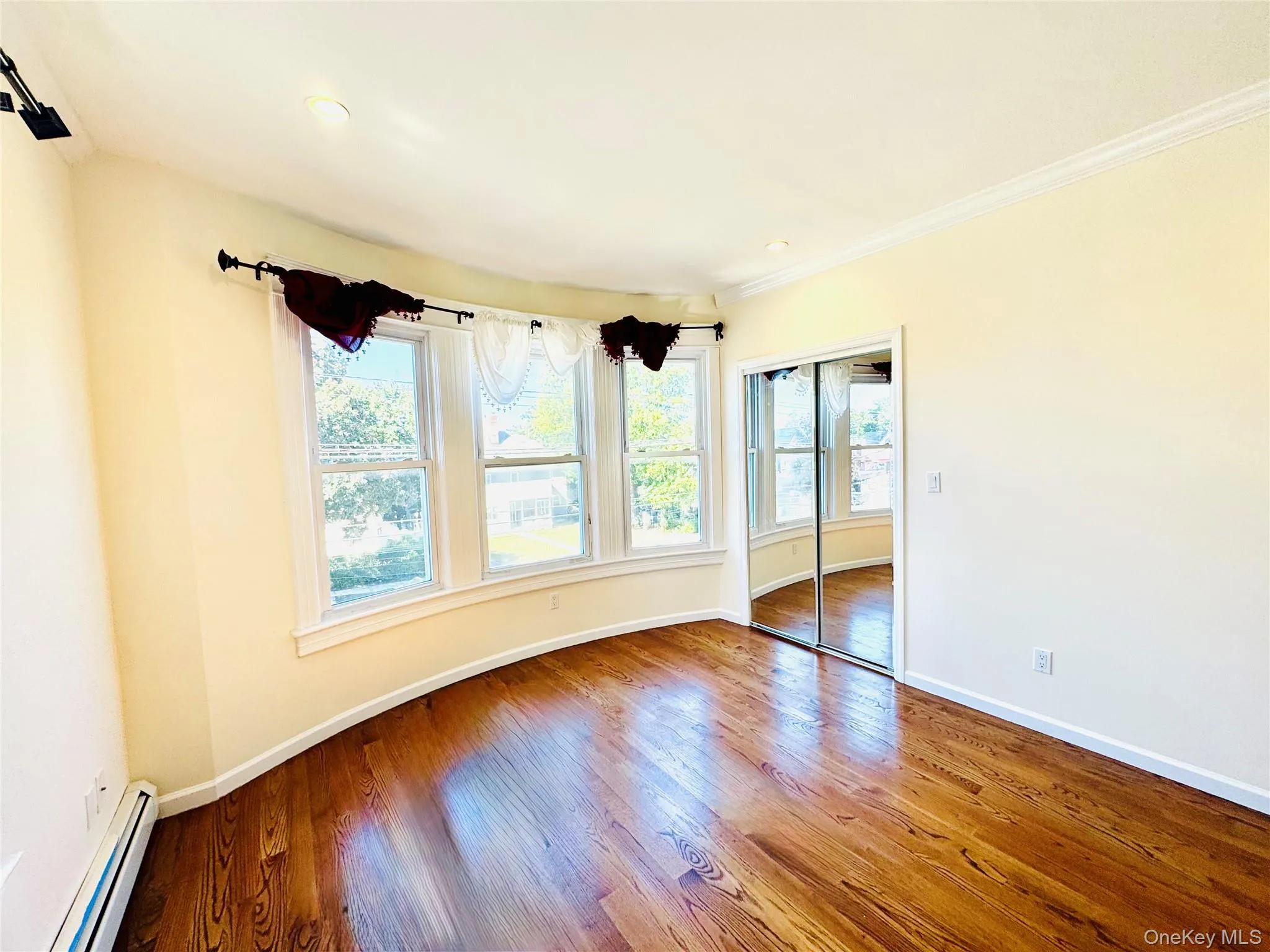 Spare room featuring plenty of natural light, a baseboard heating unit, wood-type flooring, and crown molding Spare room featuring plenty of natural light, a baseboard heating unit, wood-type flooring, and crown molding