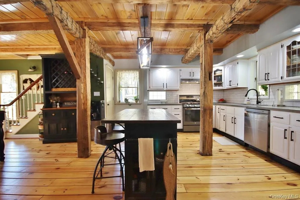 Kitchen featuring dark countertops, appliances with stainless steel finishes, a wooden ceiling with exposed beams, backsplash, and white cabinets Kitchen featuring dark countertops, appliances with stainless steel finishes, a wooden ceiling with exposed beams, backsplash, and white cabinets