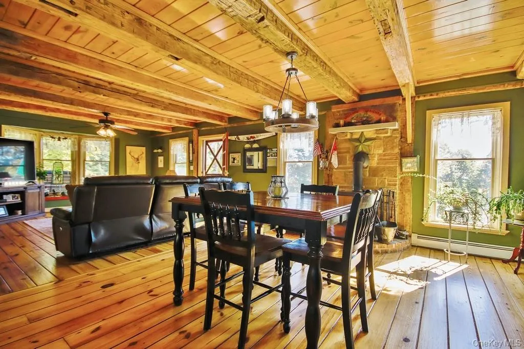 Dining space with a wood stove, light wood-type flooring, baseboard heating, a wooden ceiling with exposed beams, and ceiling fan Dining space with a wood stove, light wood-type flooring, baseboard heating, a wooden ceiling with exposed beams, and ceiling fan