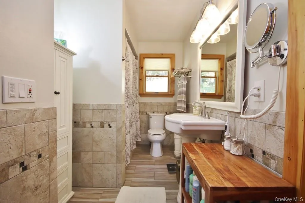 Full bathroom featuring tile walls, wainscoting, and wood finished floors Full bathroom featuring tile walls, wainscoting, and wood finished floors