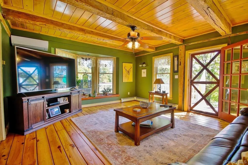 Living area with light wood-type flooring, an AC wall unit, a wooden ceiling with exposed beams, and a ceiling fan Living area with light wood-type flooring, an AC wall unit, a wooden ceiling with exposed beams, and a ceiling fan