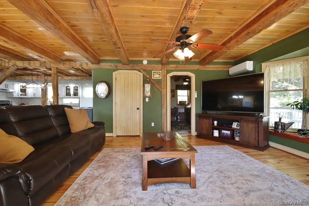 Living area with light wood-style flooring, a wood ceiling with exposed beams, arched walkways, a ceiling fan, and a wall mounted air conditioner Living area with light wood-style flooring, a wood ceiling with exposed beams, arched walkways, a ceiling fan, and a wall mounted air conditioner