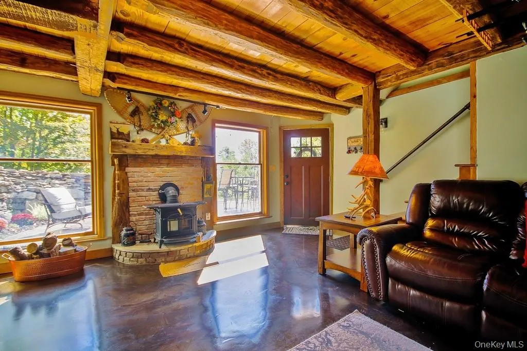 Living room with a wood stove, finished concrete floors, and a wood ceiling with exposed beams Living room with a wood stove, finished concrete floors, and a wood ceiling with exposed beams