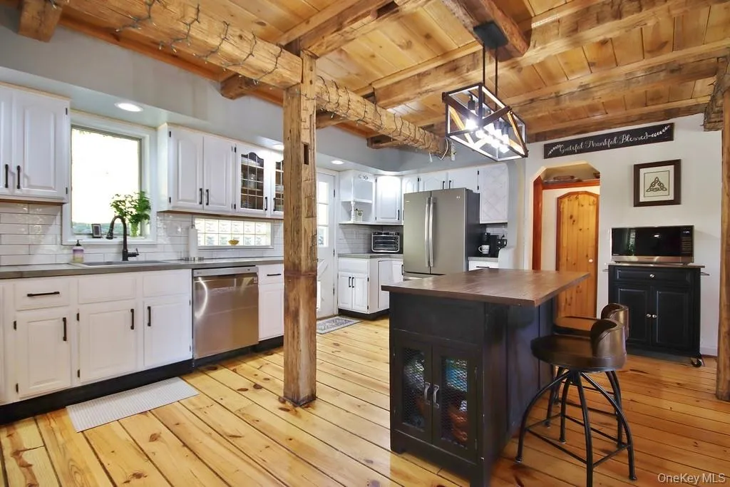 Kitchen featuring glass insert cabinets, pendant lighting, a breakfast bar area, light wood finished floors, and a wooden ceiling with exposed beams Kitchen featuring glass insert cabinets, pendant lighting, a breakfast bar area, light wood finished floors, and a wooden ceiling with exposed beams