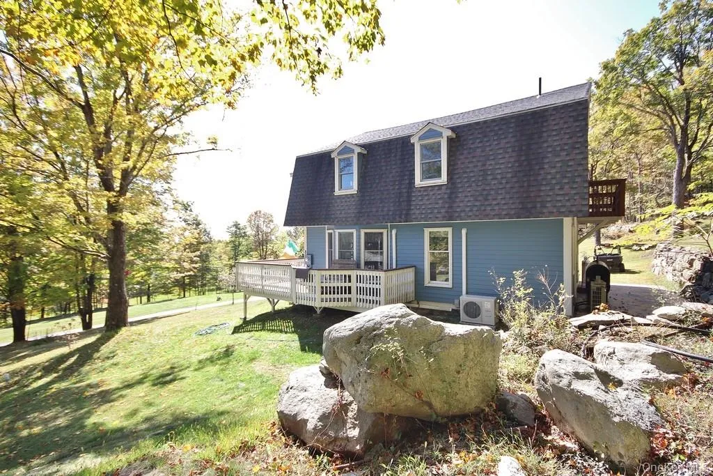 Rear view of property with a wooden deck, roof with shingles, a yard, and mansard roof Rear view of property with a wooden deck, roof with shingles, a yard, and mansard roof