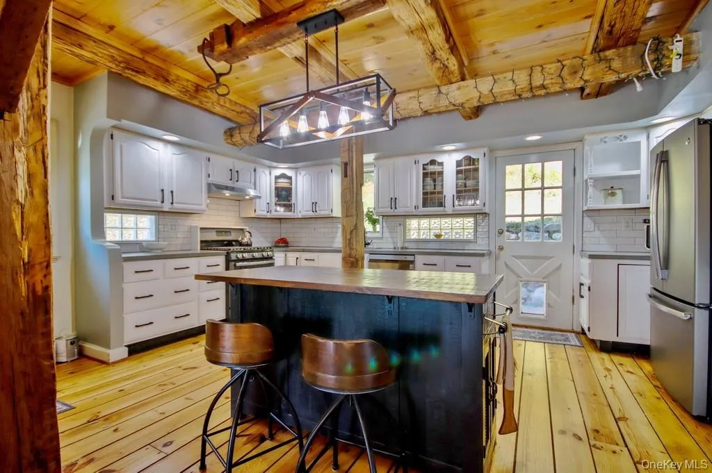 Kitchen featuring decorative backsplash, white cabinets, appliances with stainless steel finishes, a wood ceiling with exposed beams, and pendant lighting Kitchen featuring decorative backsplash, white cabinets, appliances with stainless steel finishes, a wood ceiling with exposed beams, and pendant lighting