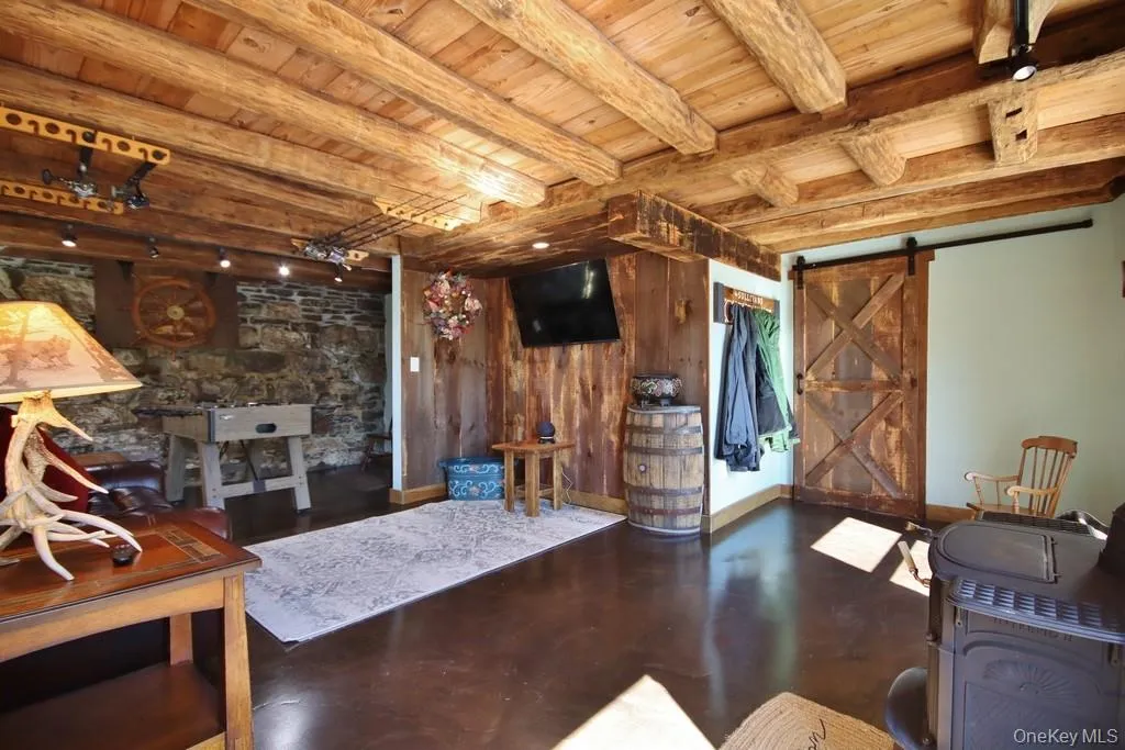 Living room featuring wood walls, a barn door, a wooden ceiling with exposed beams, and concrete flooring Living room featuring wood walls, a barn door, a wooden ceiling with exposed beams, and concrete flooring