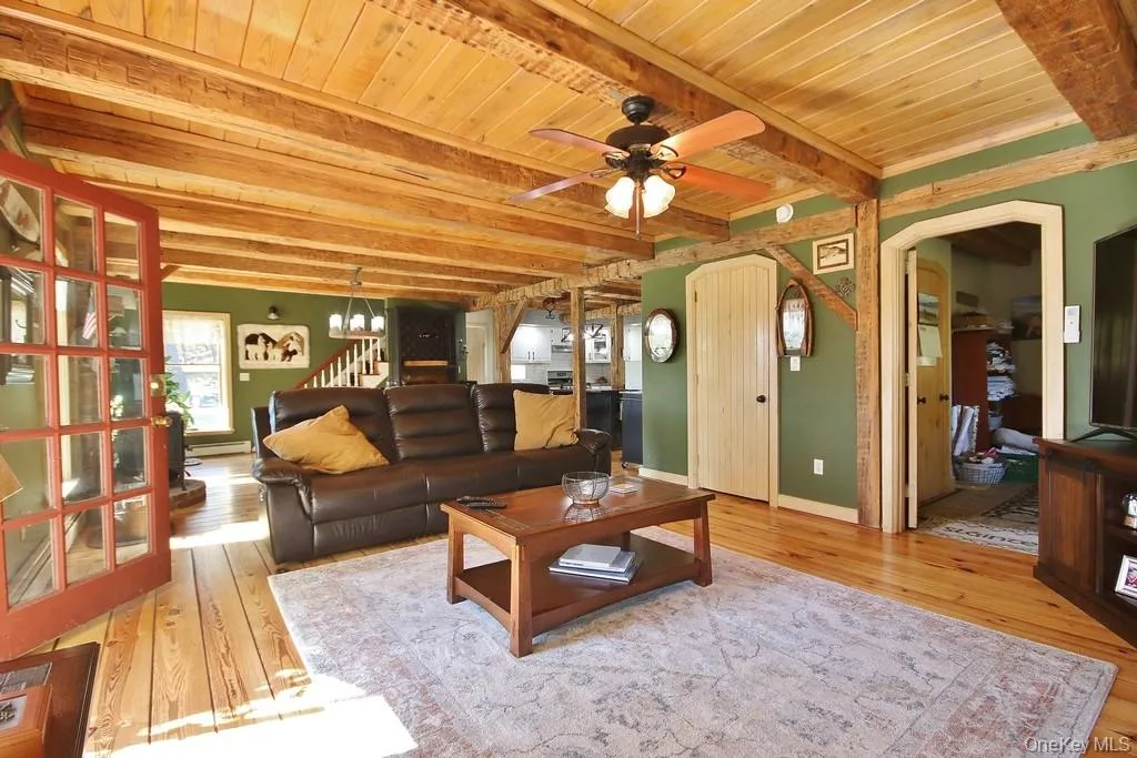 Living area with stairs, light wood-style floors, a wooden ceiling with exposed beams, a ceiling fan, and a baseboard radiator Living area with stairs, light wood-style floors, a wooden ceiling with exposed beams, a ceiling fan, and a baseboard radiator