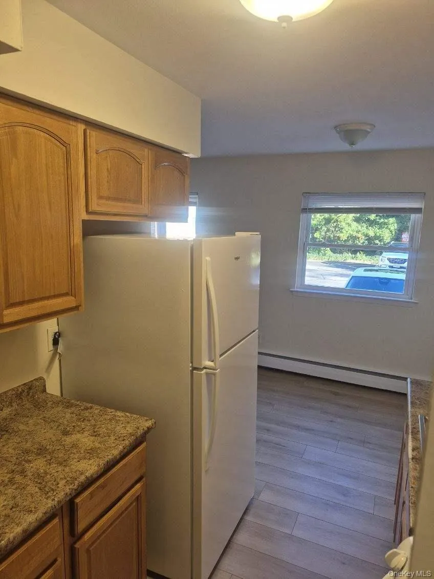 Kitchen featuring brown cabinetry, a baseboard heating unit, and freestanding refrigerator Kitchen featuring brown cabinetry, a baseboard heating unit, and freestanding refrigerator