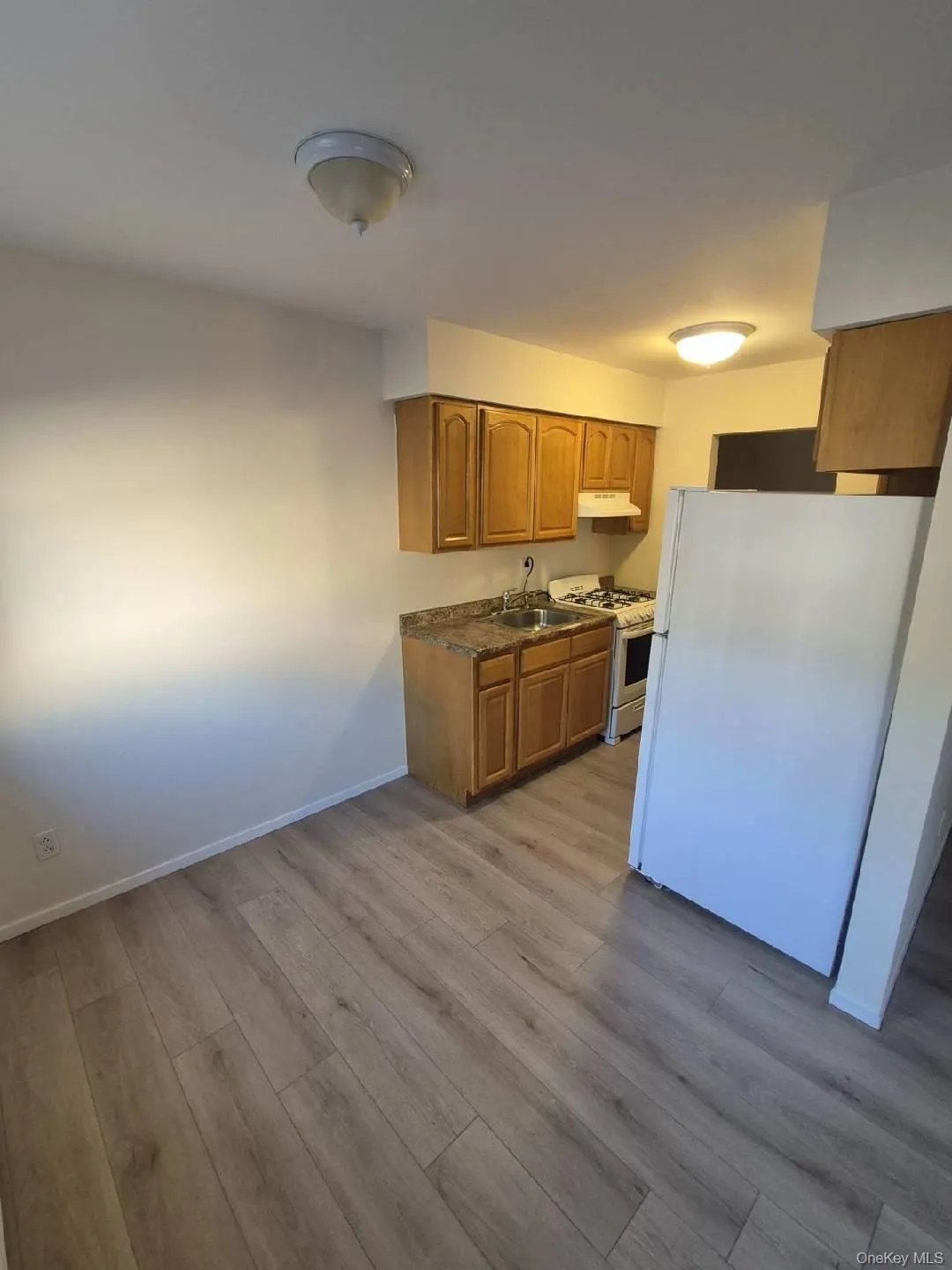 Kitchen with white appliances, brown cabinets, light wood-type flooring, and under cabinet range hood Kitchen with white appliances, brown cabinets, light wood-type flooring, and under cabinet range hood