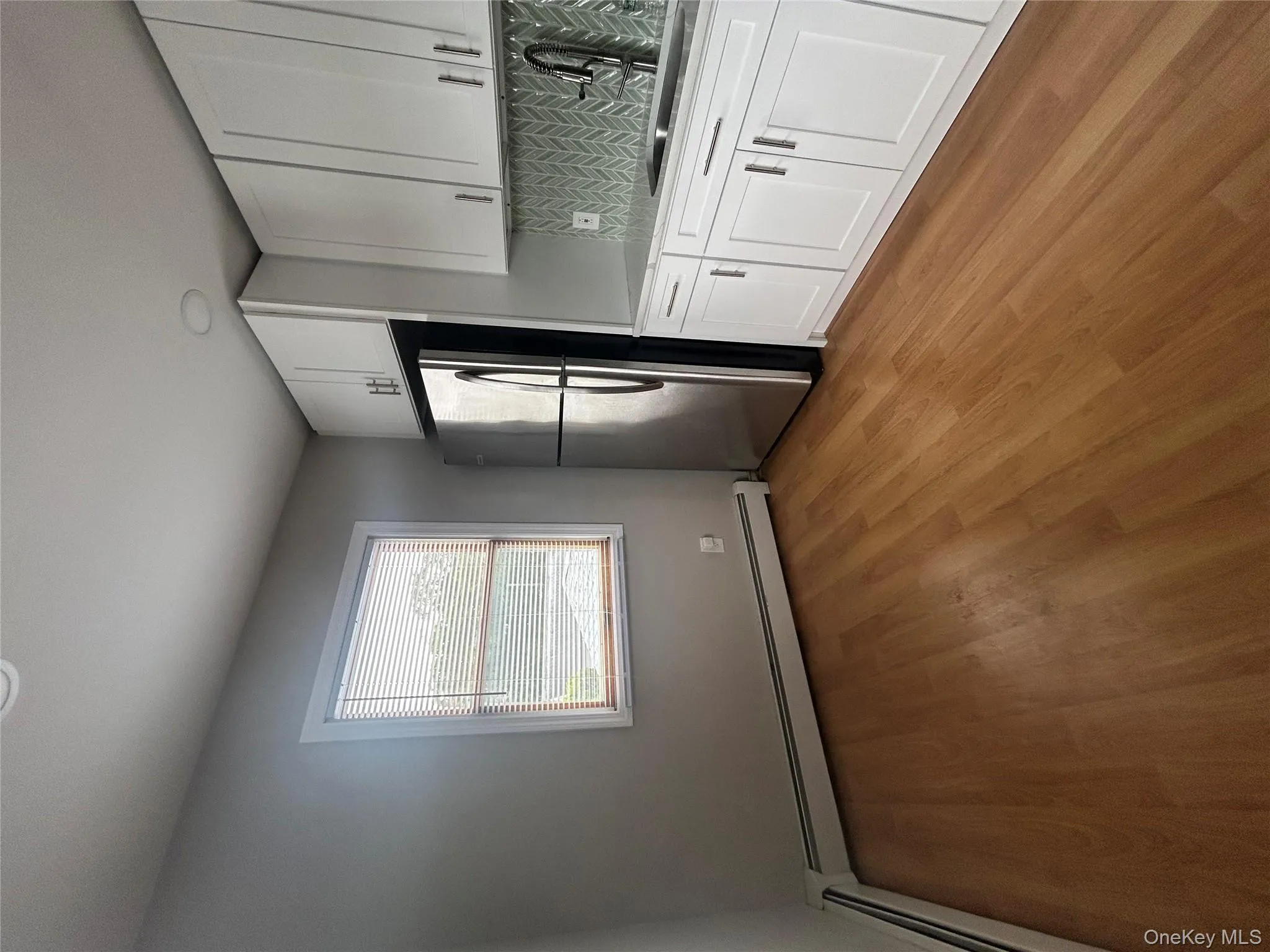 Kitchen with tasteful backsplash, white cabinets, stainless steel refrigerator, a baseboard radiator, and recessed lighting Kitchen with tasteful backsplash, white cabinets, stainless steel refrigerator, a baseboard radiator, and recessed lighting