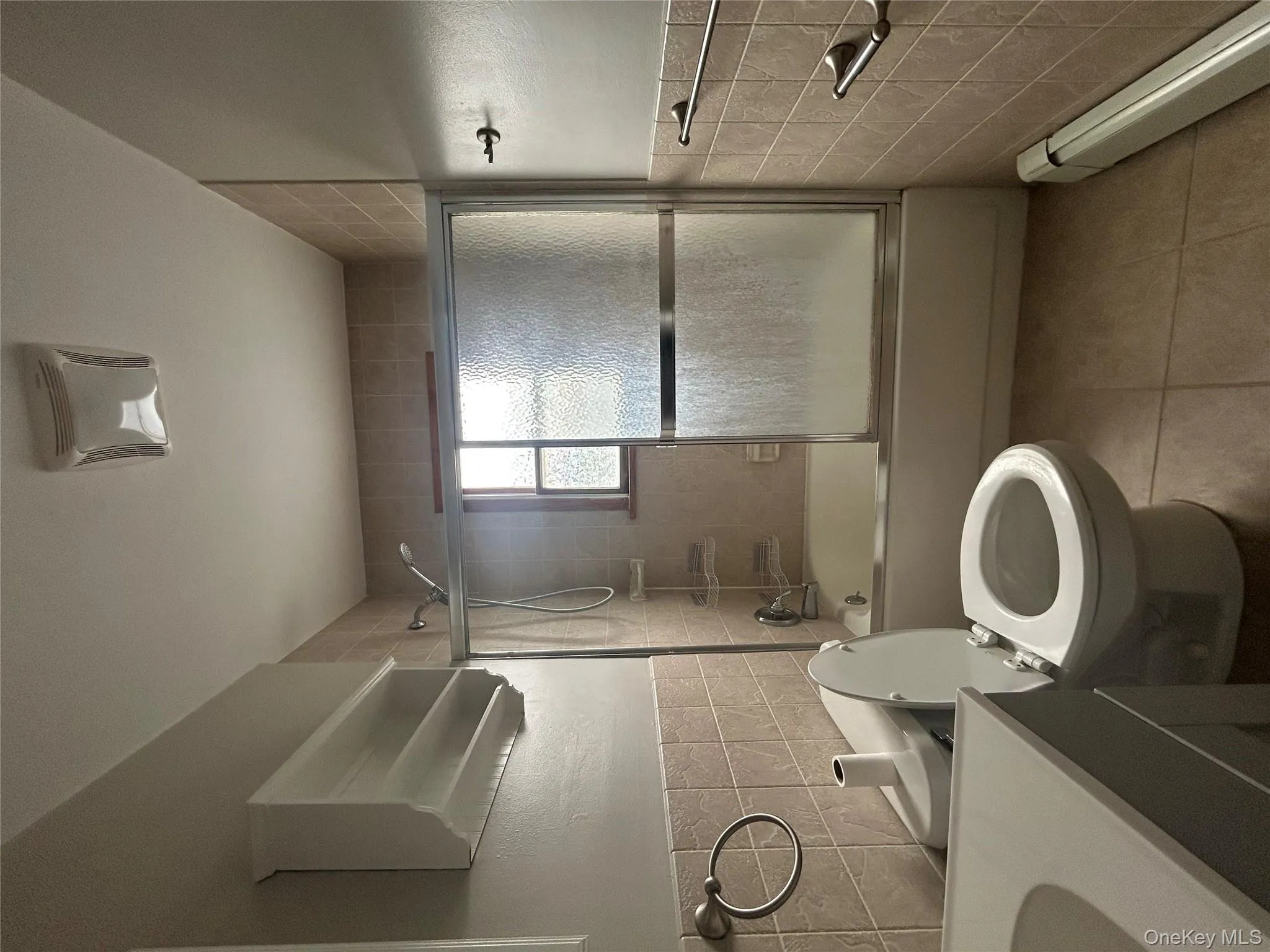 Full bath with tile walls, a baseboard heating unit, combined bath / shower with glass door, wainscoting, and vanity Full bath with tile walls, a baseboard heating unit, combined bath / shower with glass door, wainscoting, and vanity