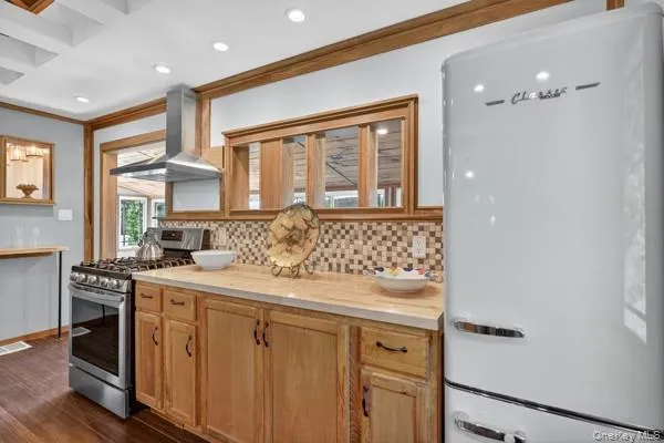 Kitchen with freestanding refrigerator, gas range, backsplash, ornamental molding, and dark wood-style floors Kitchen with freestanding refrigerator, gas range, backsplash, ornamental molding, and dark wood-style floors
