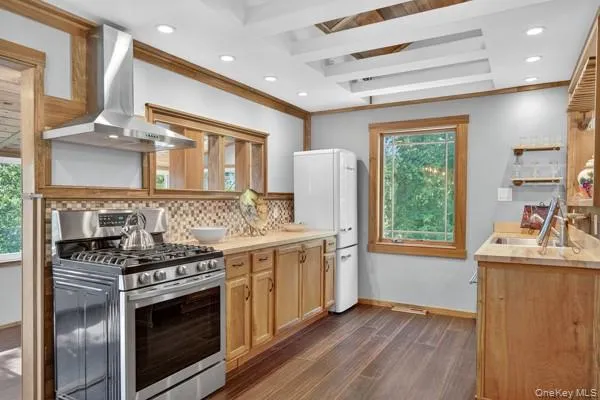 Kitchen with gas range, open shelves, light countertops, wall chimney range hood, and recessed lighting Kitchen with gas range, open shelves, light countertops, wall chimney range hood, and recessed lighting