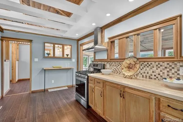Kitchen featuring stainless steel range with gas cooktop, decorative backsplash, wall chimney range hood, recessed lighting, and beamed ceiling Kitchen featuring stainless steel range with gas cooktop, decorative backsplash, wall chimney range hood, recessed lighting, and beamed ceiling